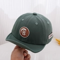 Detailed close-up of dark green cotton baby cap with embroidered B patch and side label - Green / 50cm 1-3 Years