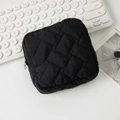 Macro detail of black quilted square makeup bag with smooth silver zipper on a white desk - Black