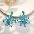 Macro shot of teal hand-woven raffia flower earrings with intricate hollow daisy details - Blue
