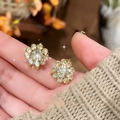 Elegant gold plated sunflower crystal stud earrings held by hand on floral background - Gold (Silver Earring Post)