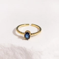 Detailed shot of an adjustable gold ring with blue oval stone on white textured rock - Deep Blue Gemstone Gold Base