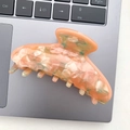Detailed close-up of an orange acetate hair claw clip with colorful marble pattern on a keyboard - Orange