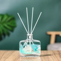 Square glass diffuser bottle with blue feathers and white rattan sticks on wood - Wild Bluebell - 100ml