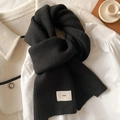 Close-up of soft black knitted scarf with emo logo tag on wool coat background - Black