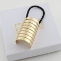 Close-up of golden striped metal hair cuff with elastic band on a white textured box - Gold Small
