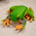 Plüschfrosch in Grün mit orange-blauen Gradienten-Extremitäten auf warmem Teppich - 28cm (Klein) / Grün (Frosch)