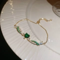 Detalle de la pulsera dorada elegante con circón de corazón verde en plato de cerámica - Oro-Verde