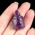 Miniature amethyst turtle carving shown on fingertip to display its tiny size and deep purple color - Amethyst