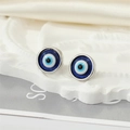 Close-up of sparkling resin Evil Eye stud earrings on a white embossed tray - Silver Blue Eye