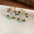 Detail of beaded hoop earrings with tiger eye, cat's eye stone, and pearls on a velvet tray - Gold Brown