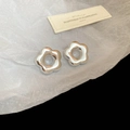 Detail of silver metallic flower stud earrings on white crinkled paper backdrop - Silver Hollow Flower (Stainless Steel Pin)