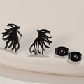 Detail of matte black tree branch earrings with butterfly backs on a stone texture - Black