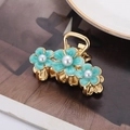 Pinza para el cabello dorada con flores de esmalte verde y perlas sobre una revista - Azul Cielo