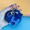 Close-up of blue pompom keychain with sequin letter H charm and gold lobster clasp - Letter H