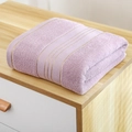 Plush light purple cotton bath towel with gold trim stripes folded on wooden surface - 140x70cm / Pink