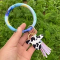Gros plan du porte-clés bracelet bleu marbré avec pendentif vache et pompon violet - Peinture à l'Encre