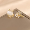 Asymmetric gold cat opal and pearl flower stud earrings set on a leather display - Cat's Eye + Golden Flower