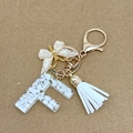 Letter F keychain with white stones, gold butterfly charm and white tassel on brown paper - Letter F