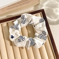 White floral lace scrunchie with blue pattern and Mickey silhouette in a beige jewelry tray - Label Grid