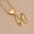 Macro shot of gold letter H necklace with colorful cubic zirconia and heart link - Letter H / Gold