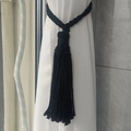 Detail of handwoven black cotton curtain tieback with dense fringe on a white drape - Black
