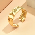 Irregular hammered gold cuff bracelet with molten texture on a pink geometric background - Gold