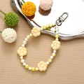 Close-up of yellow flower beads and white pearls mobile chain on a silver tray - Yellow