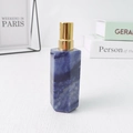 Blue hexagonal natural crystal perfume bottle with gold pump on white wood table - Blue Aventurine
