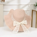 Detail of pink straw sun hat featuring large white lace floral bow and wavy brim design - Plum Wave Pink