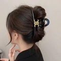 Elegant black resin hair claw clip with gold metal buckle detail shown in a hair bun - Frosted Double C Logo
