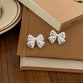 Close-up of silver bow earrings with textured finish on a vintage book background - Silver Pleated Texture Bow Stud Earrings (A-139)