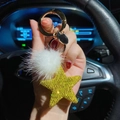 Hand hält gelben funkelnden Stern-Schlüsselanhänger mit weißem Pelzball im Auto - Gold