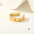 Close-up of golden adjustable star ring with orange enamel drips on a stone surface - Orange Stars (RG0441-E)