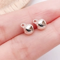 Zwei kleine polierte silberne Metallglocken-Anhänger auf einer Fingerspitze präsentiert - 6mm / Hellsilber