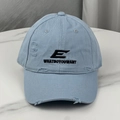 Gros plan détaillé de la casquette bleu clair délavée avec logo E brodé et déchirures - Bleu