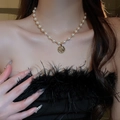 Gros plan d'un collier de perles blanches avec un pendentif pièce dorée sur un cou - Collier de Perles Pièce en Relief Or / 10# Collier-Or