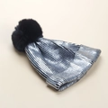 Detail of winter knit hat featuring silver metallic fibers and a fluffy faux fur pom-pom - Silver