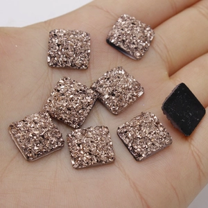 Macro detail of 12mm square rose gold glitter resin stones held in hand for size context