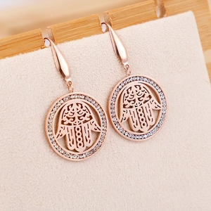 Rose gold Hamsa hand earrings with clear crystals on a beige display stand