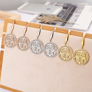 Three pairs of Hamsa hand earrings in gold, rose gold, and silver on a wood stand