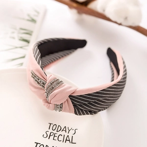 Pink and black striped fabric headband with rhinestone knot detail on a white dish