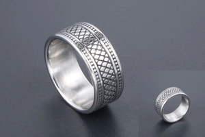 Vue macro d'une bague en acier argenté avec texture géométrique en losange et bords perlés