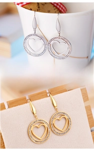 Détail de boucles d'oreilles cœur en or et argent avec strass sertis dans des cadres ronds