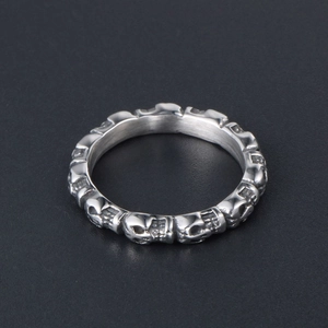 Polished titanium steel ring with continuous skull pattern on a textured black background