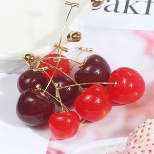 Macro detail of glossy resin cherry earrings with golden metal stems on a white background