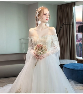 Close-up of ivory wedding dress with off-shoulder lace embroidery and sheer long sleeves