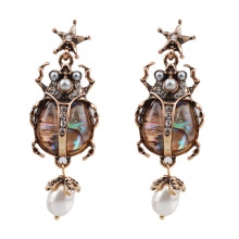 Dettaglio degli orecchini vintage a scarabeo in bronzo con inserti in madreperla e perle