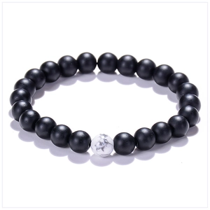 Detail of matte black beads and a single white marble textured stone on a beaded bracelet