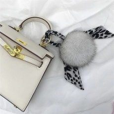 Close-up of a white leather trapezoid handbag with grey fur pompom and leopard print scarf