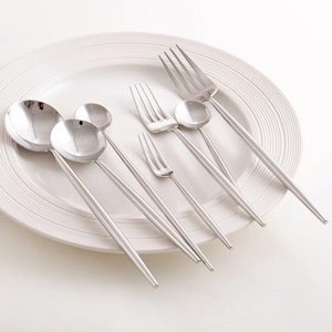 Silver 304 stainless steel cutlery set with spoons and forks on a white ceramic plate